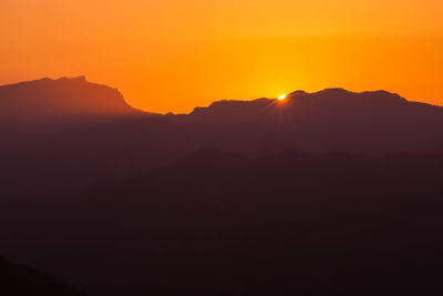 Scenic view of silhouette mountains against orange sky