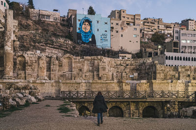 Rear view of woman walking towards built structure in city