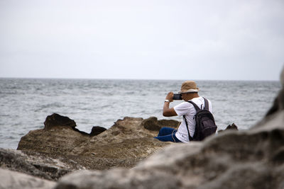 Man sitting on rock by sea against sky