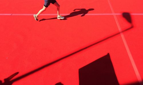 Low section of man running on red court during sunny day