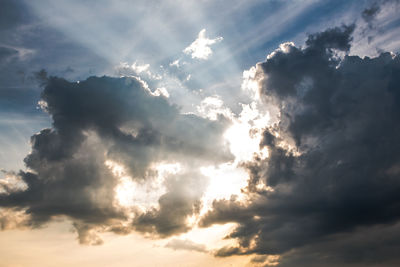Low angle view of sunlight streaming through clouds