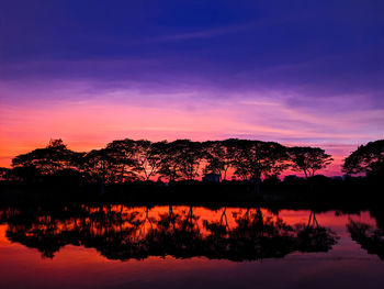 Silhouette trees by lake against romantic sky at sunset