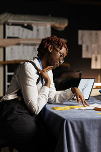 Side view of young woman using laptop at home