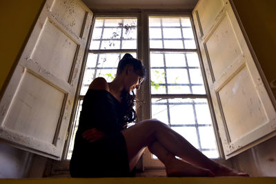 Young woman looking through window at home