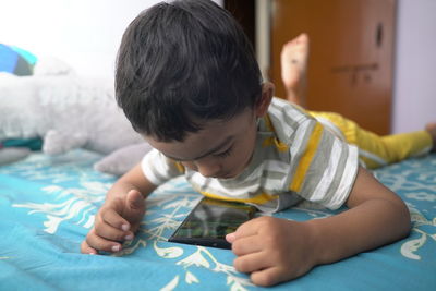 Boy watching smart phone while lying on bed