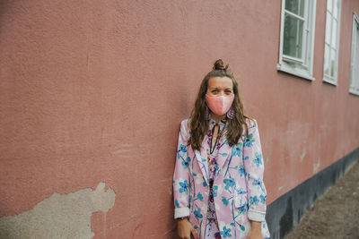 Woman wearing face mask standing against wall