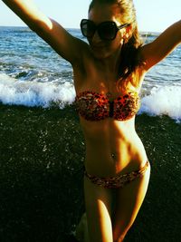 Midsection of young woman with sunglasses standing at beach