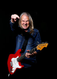 Portrait of young man playing guitar against black background