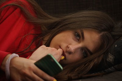 Close-up portrait of woman holding mobile phone while lying on bed at home