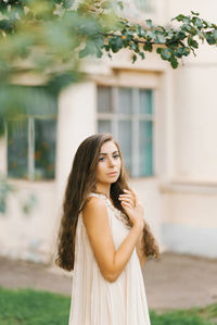 A romantic young woman in a summer dress enjoys a summer day standing near a tree 