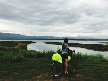 Rear view of man with bicycle on lake against sky