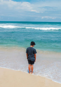 Rear view of man standing on beach against sky