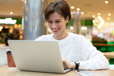 Smiling woman using laptop at mall