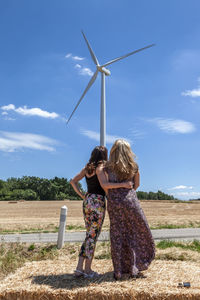 Two beautiful women travelers while taking pictures with a wind turbine in the background