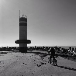 Man riding bicycle by lighthouse against clear sky