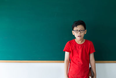 Portrait of boy wearing eyeglasses standing against blackboard in classroom