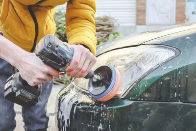 A young man polishes the headlights of a car.