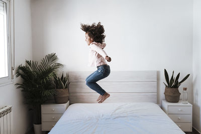 Cute girl jumping on bed in bedroom at home