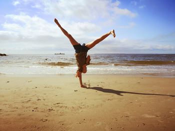 Full length of woman practicing handstand at beach against sky