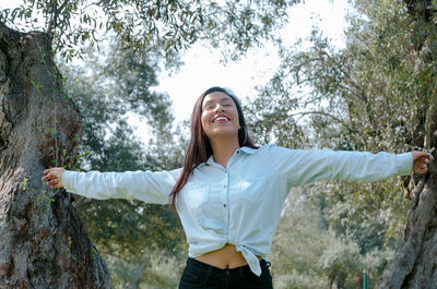 Happy young woman standing against trees