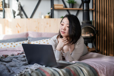 Young woman using mobile phone while sitting on bed