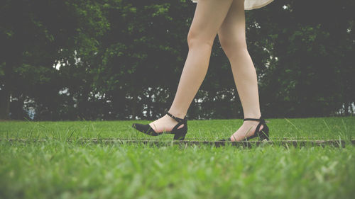 Low section of woman walking on grassy field