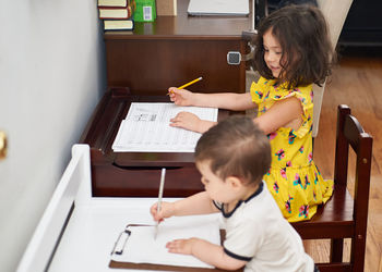 Little toddler copying his sister doing her homework