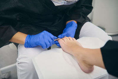 Cropped unrecognizable female podologist in uniform doing pedicure for woman sitting in medical chair in beauty clinic