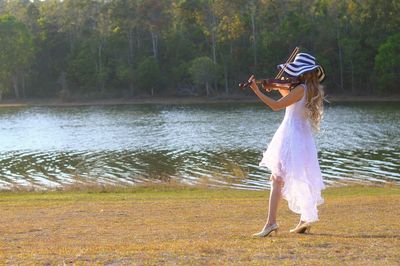 Side view of woman playing violin while standing on lakeshore