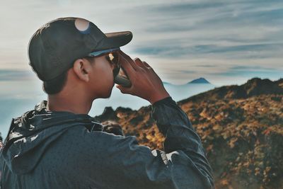 Side view of young man drinking while standing against landscape