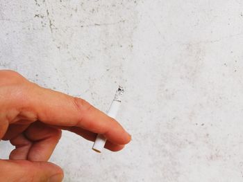 Midsection of person holding cigarette against wall