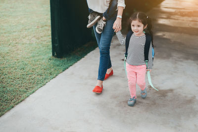 Low section of mother walking with daughter on footpath