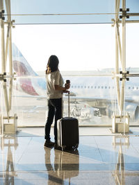 Young woman standing with baggage near the airport window waiting for the flight