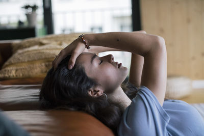 Side view of depressed woman with hand in hair reclining on sofa at home