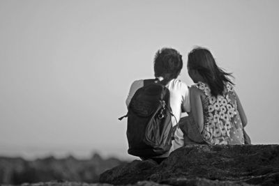 Rear view of couple sitting on rock against clear sky