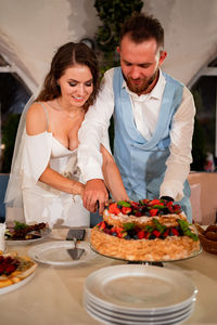 Newlywed couple cutting cake at home