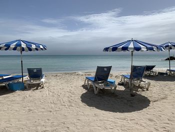 Deck chairs on beach against sky