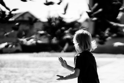 Rear view of boy with pigeons flying in background