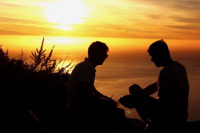 Silhouette couple sitting against orange sky during sunset
