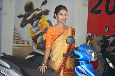Portrait of smiling woman wearing sari standing by motorcycle