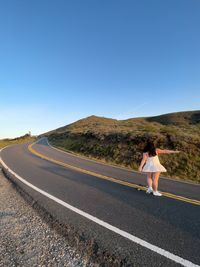 Rear view of girl walking on road against clear blue sky