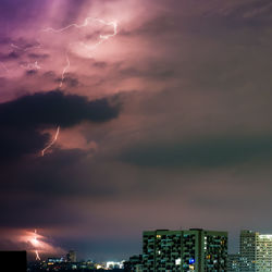 Aerial view of illuminated city against dramatic sky at night