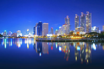 Reflection of illuminated buildings in lake against blue sky