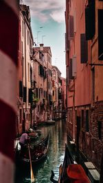 Man rowing gondola in canal amidst buildings