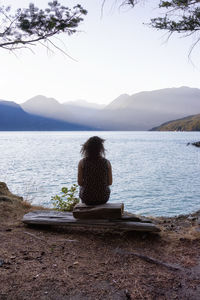 Rear view of woman sitting on mountain against sky