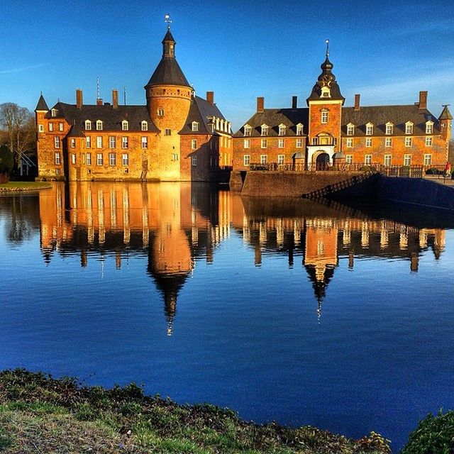 architecture, building exterior, built structure, water, reflection, city, sky, blue, history, travel destinations, famous place, river, waterfront, building, outdoors, tourism, illuminated, travel, residential building, no people