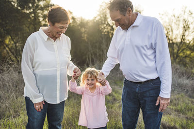 Portrait of grandparents holding little girls hand in field  person