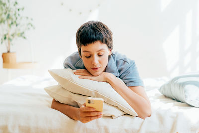 Young woman reading book while sitting on bed at home
