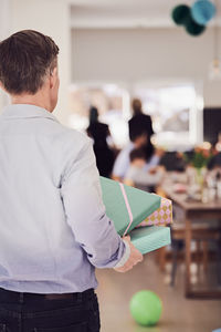 Rear view of senior man holding gift boxes at home