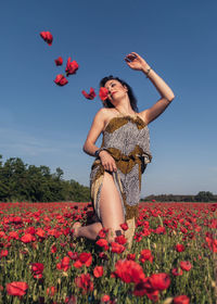 Woman with red flowers on field against sky